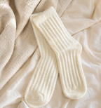 A pair of cream-colored ribbed knit socks laid flat on a soft beige blanket and white fabric background.